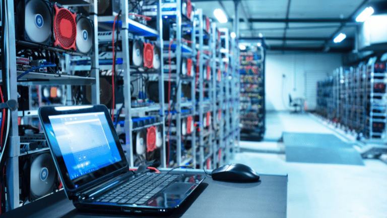 Laptop sits on a table in a room filled with rows of servers.
