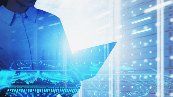 Person using a laptop with holographic data charts and server racks in the background.